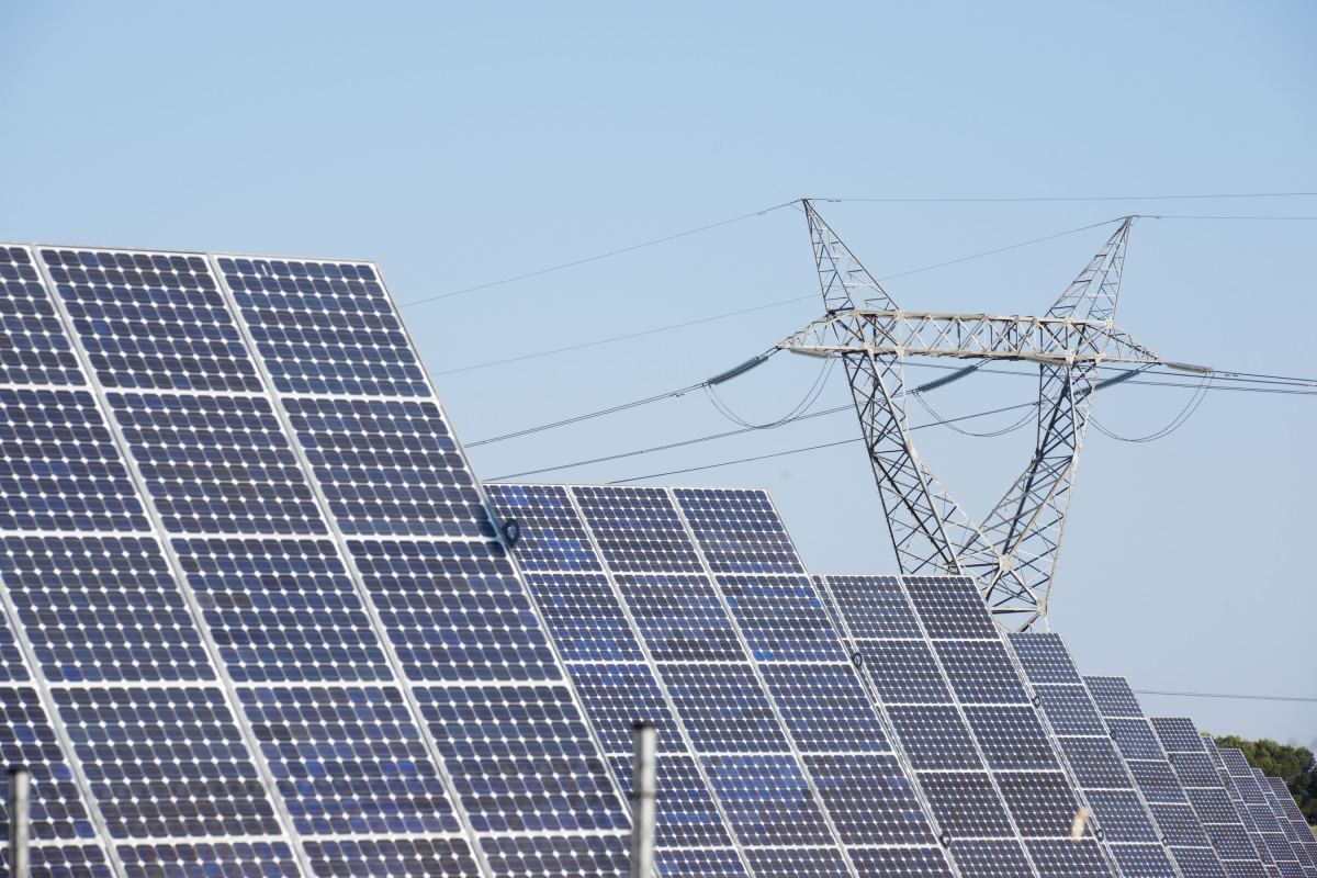 Solar panels stand in front of a high-voltage power line.