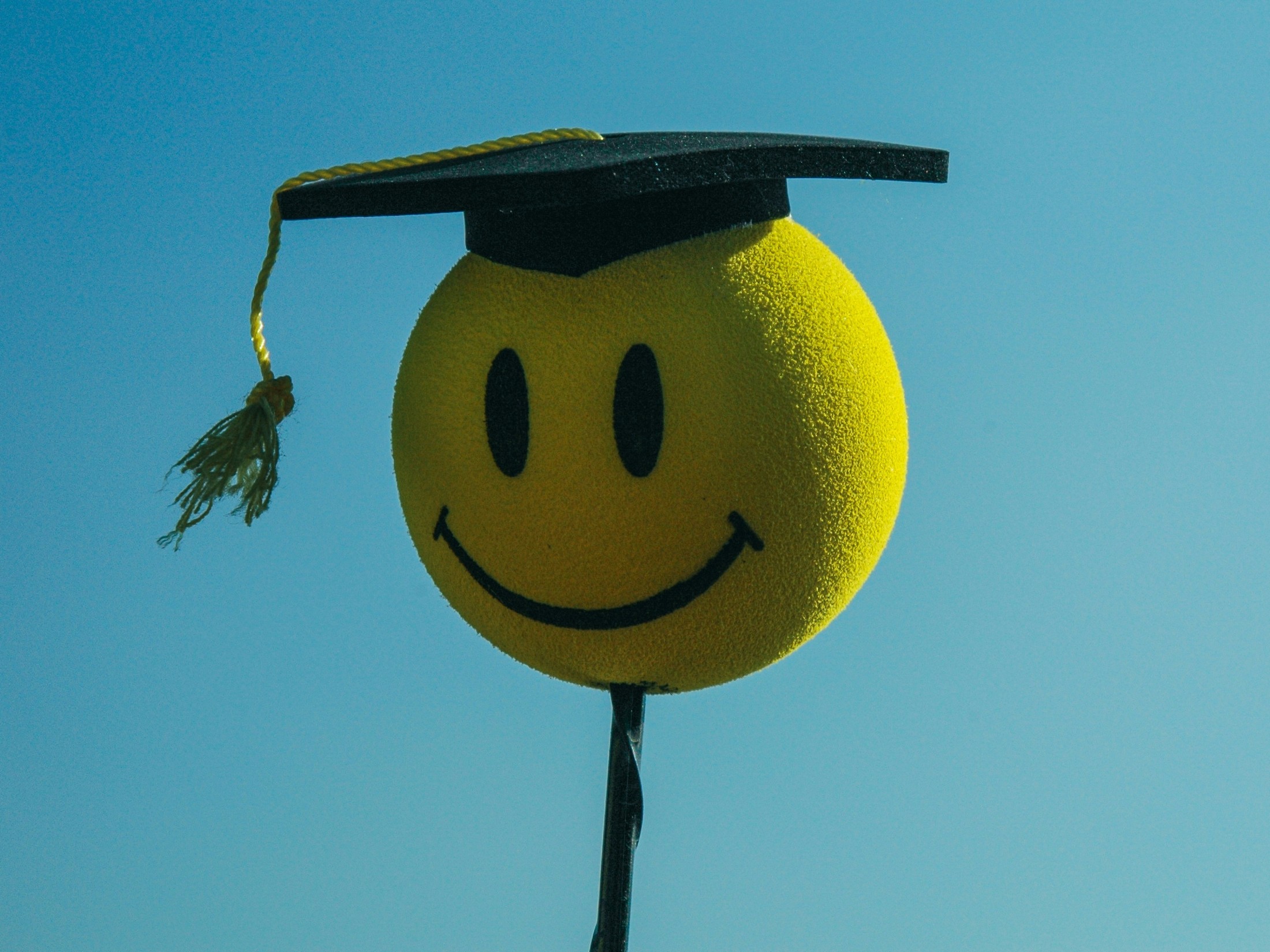 A smiley face wearing a graduation cap illustrating Carl by the Autoscience Institute, the first AI system crafting academic research papers to pass a rigorous double-blind peer-review process and raising questions about ethics including the role of artificial intelligence in academic settings.